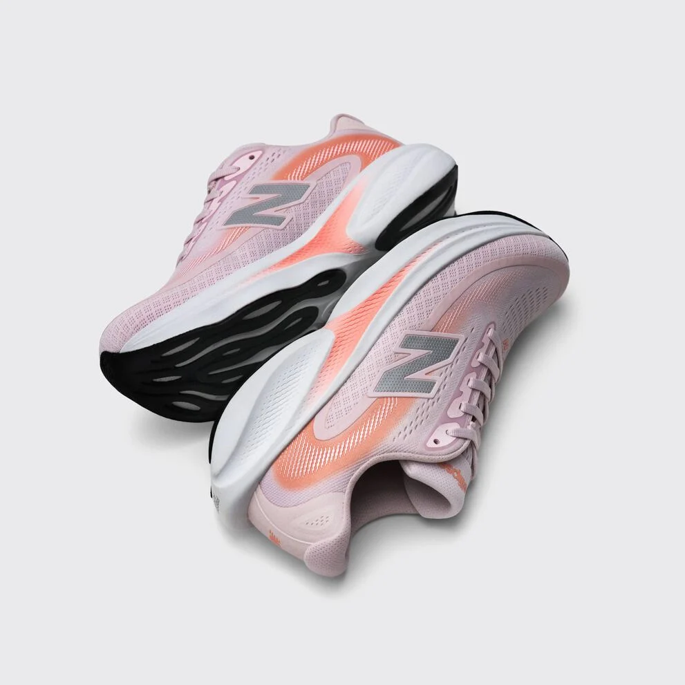 Pair of light pink New Balance running shoes with coral accents and chunky black-and-white soles displayed on a light gray background.